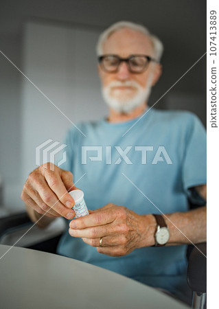 Senior man reading the usage instructions on a pill bottle label. 107413889