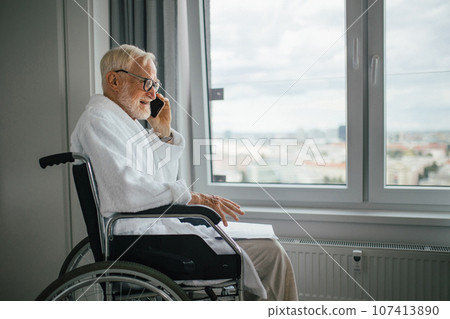 Elderly man in a wheelchair making call in his robe in the morning. 107413890