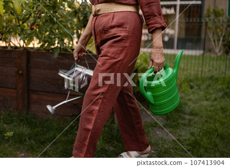 The gardener holding a plastic and metal watering can. 107413904