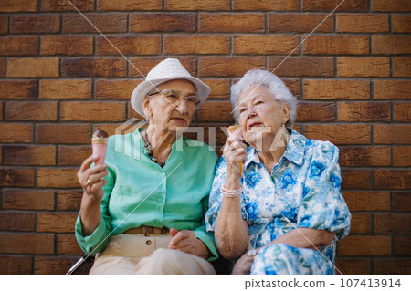 Portrait of two senior female friends in the city, eating ice cream on a hot summer day. 107413914