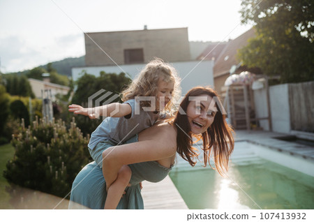 The mom is giving her little boy a piggyback ride in the garden. 107413932
