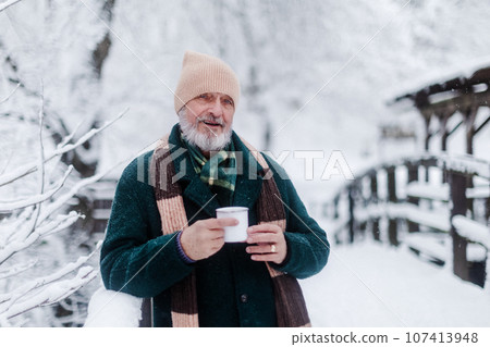 Portrait of elegant senior man drinking hot tea outdoors, during cold winter snowy day. 107413948