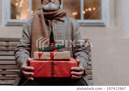Senior man sitting on a bench, holding a lot of Chrismtas gifts in his hands 107413967