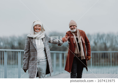 Elegant senior couple walking near the river, during cold winter day. Elegant senior couple walking near the river, during cold winter day. 107413975