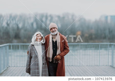 Elegant senior couple walking near the river, during cold winter day. 107413976