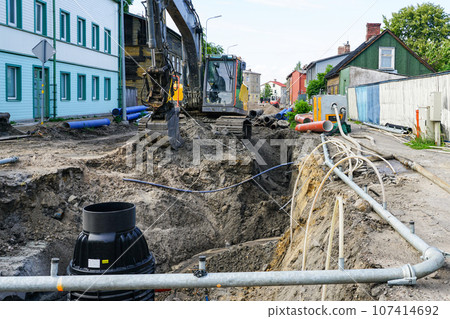 Street reconstruction view, deep trench, dewatering system, new and old pipes, excavator Street reconstruction view, deep trench, dewatering system, new and old pipes, excavator 107414692