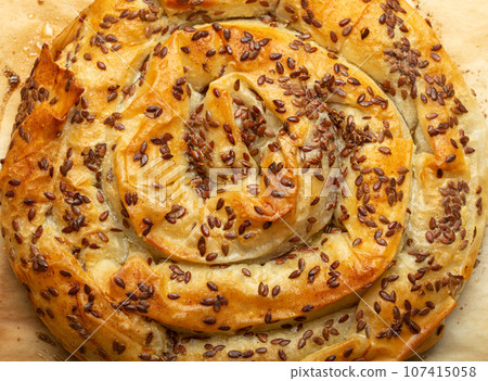 Freshly baked Burek made of filo dough with filling on baking paper background top view. Traditional savoury spiral pie of Balkans, Middle East and Central Asia 107415058