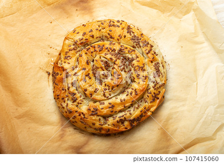 Freshly baked Burek made of filo dough with filling on baking paper background top view. Traditional savoury spiral pie of Balkans, Middle East and Central Asia 107415060
