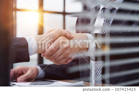 executives shaking hands in front of their manager and a colleague executives shaking hands in front of their manager and a colleague 107415423
