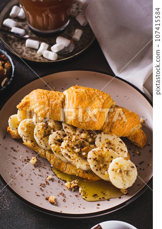 Croissant sandwich with banana, honey and nuts on a plate on the table vertical view Croissant sandwich with banana, honey and nuts on a plate on the table vertical view 107415584