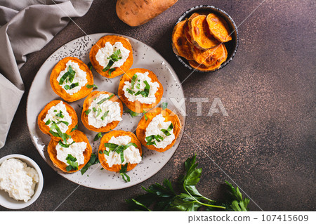 Pieces of baked sweet potato with ricotta and herbs on a plate on the table top view 107415609