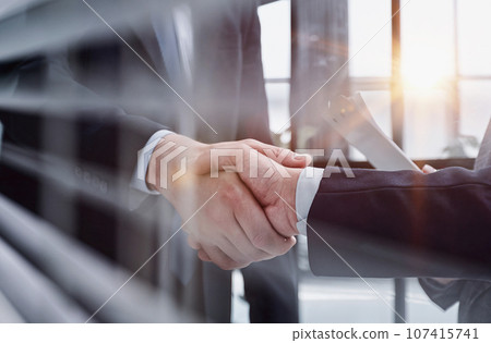 executives shaking hands in front of their manager and a colleague executives shaking hands in front of their manager and a colleague 107415741