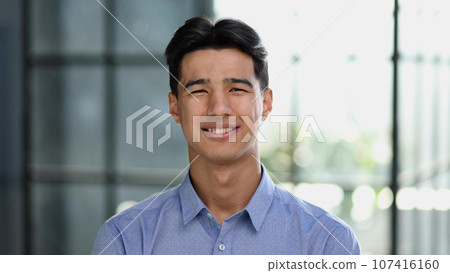 Well dressed young Asian businessman smiling confidently while standing alone in a bright modern office 107416160