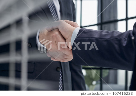 executives shaking hands in front of their manager and a colleague executives shaking hands in front of their manager and a colleague 107416228