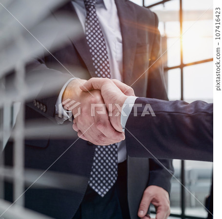 executives shaking hands in front of their manager and a colleague 107416423