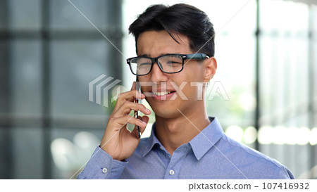 Businessman making a phone call while standing in the lobby of a modern office 107416932