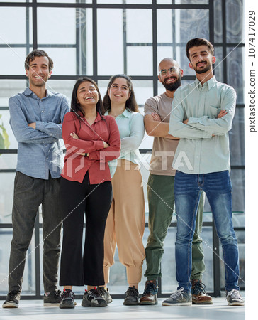 multicultural businessmen and cheerful businesswomen standing with crossed arms and looking at camera 107417029
