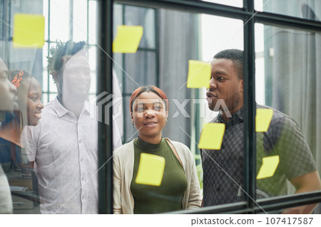 a team of young designers sticking notes on glass in a modern office a team of young designers sticking notes on glass in a modern office 107417587
