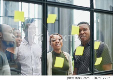 a team of young designers sticking notes on glass in a modern office a team of young designers sticking notes on glass in a modern office 107417726