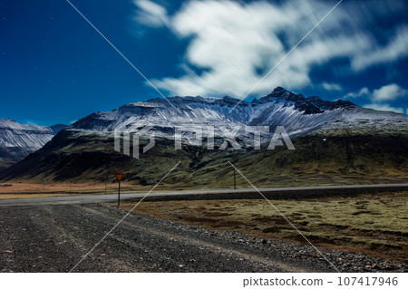 Majestic region with mountains covered in snow, night photography theme. Gorgeous highway landscape with icy peaks and glacial slopes in icelandic greenery, dramatic skyline view. Majestic region with mountains covered in snow, night photography theme. Gorgeous highway landscape with icy peaks and glacial slopes in icelandic greenery, dramatic skyline view. 107417946