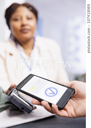 Contactless smartphone payment. African American woman cashier holding pos terminal checking out customer in retail store. Close up of male hand holding cellphone paying with mobile device Contactless smartphone payment. African American woman cashier holding pos terminal checking out customer in retail store. Close up of male hand holding cellphone paying with mobile device 107418069