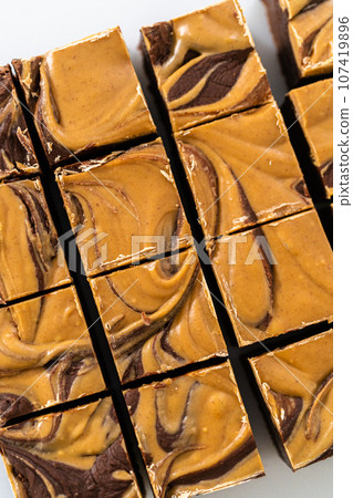 Cutting chocolate fudge with peanut butter swirl into small pieces on a white cutting board. 107419896