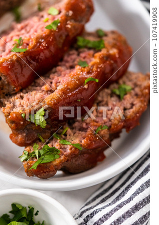 Slicing classic meatloaf with a sweet glaze on a white serving plate 107419908