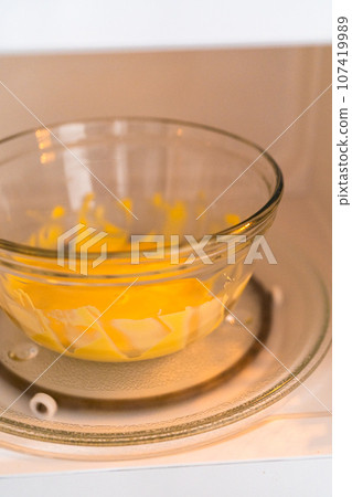 Melting yellow chocolate chips in a glass mixing bowl in a microwave. 107419989