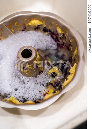 Soaking dirty aluminum bundt cake pan with soapy water in a kitchen sink. Soaking dirty aluminum bundt cake pan with soapy water in a kitchen sink. 107419992