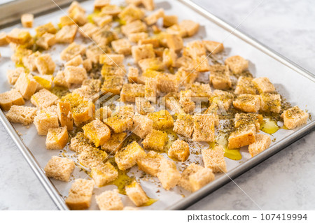 Baking croutons seasoned with olive oil and spiced on a baking sheet lined with parchment paper. Baking croutons seasoned with olive oil and spiced on a baking sheet lined with parchment paper. 107419994