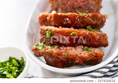 Slicing classic meatloaf with a sweet glaze on a white serving plate 107420018