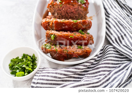 Slicing classic meatloaf with a sweet glaze on a white serving plate Slicing classic meatloaf with a sweet glaze on a white serving plate 107420020