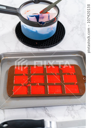 Filling silicone mold with red and blue melted chocolate to make chocolate stars for patriotic lemon cupcakes. Filling silicone mold with red and blue melted chocolate to make chocolate stars for patriotic lemon cupcakes. 107420138