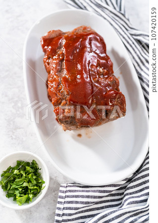 Slicing classic meatloaf with a sweet glaze on a white serving plate Slicing classic meatloaf with a sweet glaze on a white serving plate 107420159