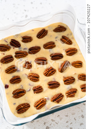 Pouring fudge mixture into the baking pan lined with parchment paper to prepare white chocolate cranberry pecan fudge. 107420227