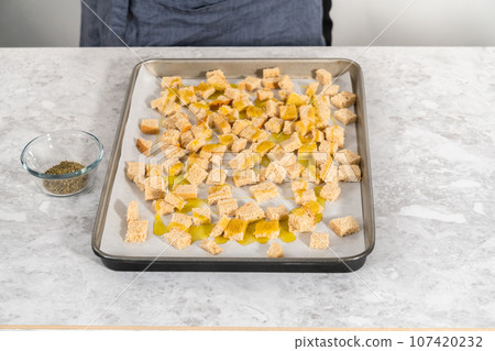 Baking croutons seasoned with olive oil and spiced on a baking sheet lined with parchment paper. 107420232
