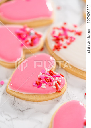 Decorating heart-shaped sugar cookies with pink and white royal icing for Valentine's Day. 107420233