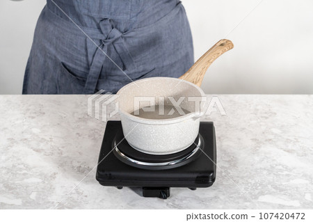 Melting white chocolate chips in a stainless steel double boiler pot over a cooking pot with hot water. 107420472