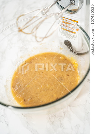 Mixing ingredients in a large glass mixing bowl to bake banana oatmeal muffins. 107420529