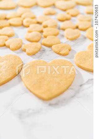 Decorating heart-shaped sugar cookies with pink and white royal icing for Valentine's Day. 107420683