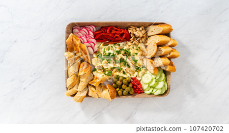 Flat lay. A large vegetarian party butter board with fresh and pickled vegetables and sliced french baguette for a party. Flat lay. A large vegetarian party butter board with fresh and pickled vegetables and sliced french baguette for a party. 107420702