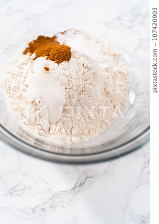 Mixing dry ingredients in a large glass mixing bowl to bake soft oatmeal raisin walnut cookies. 107420903