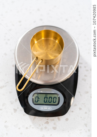 Measuring chocolate chips in a metal measuring cup on the kitchen scale. Measuring chocolate chips in a metal measuring cup on the kitchen scale. 107420985