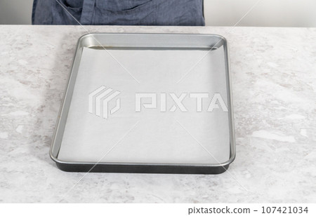 Spreading bread crumbs on a baking sheet lined with parchment paper to prepare dried bread crumbs. 107421034