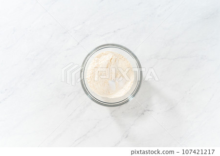 Flat lay. Mixing dry ingredients with a hand whisk in a glass mixing bowl to bake lemon blueberry bundt cake. Flat lay. Mixing dry ingredients with a hand whisk in a glass mixing bowl to bake lemon blueberry bundt cake. 107421217