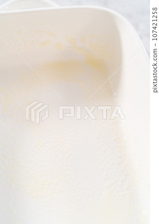 Greasing white casserole dish to bake bread pudding. Greasing white casserole dish to bake bread pudding. 107421258