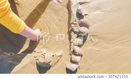 Little girl joyfully clamming on Pismo Beach, bundled up for the winter chill as she explores the sands for seashells and clams. 107421333