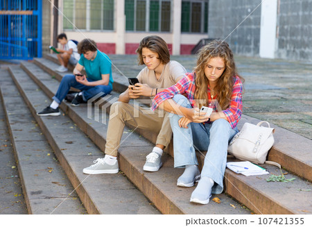 Girl and boy write messages on smartphone on street 107421355