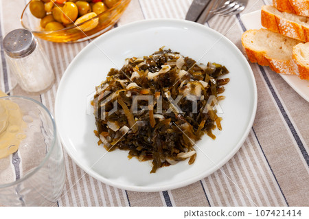 Appetizing marinated seaweed salad with onion served in plate with cutlery and bread 107421414