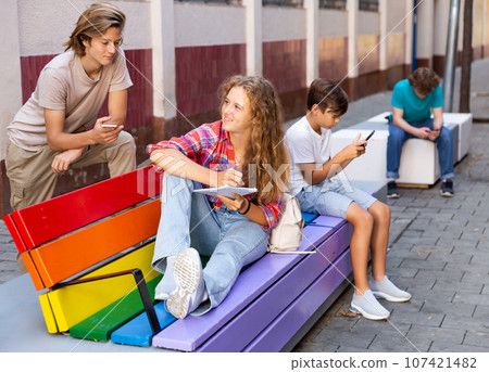 Group of teenagers sitting on bench outdoors 107421482